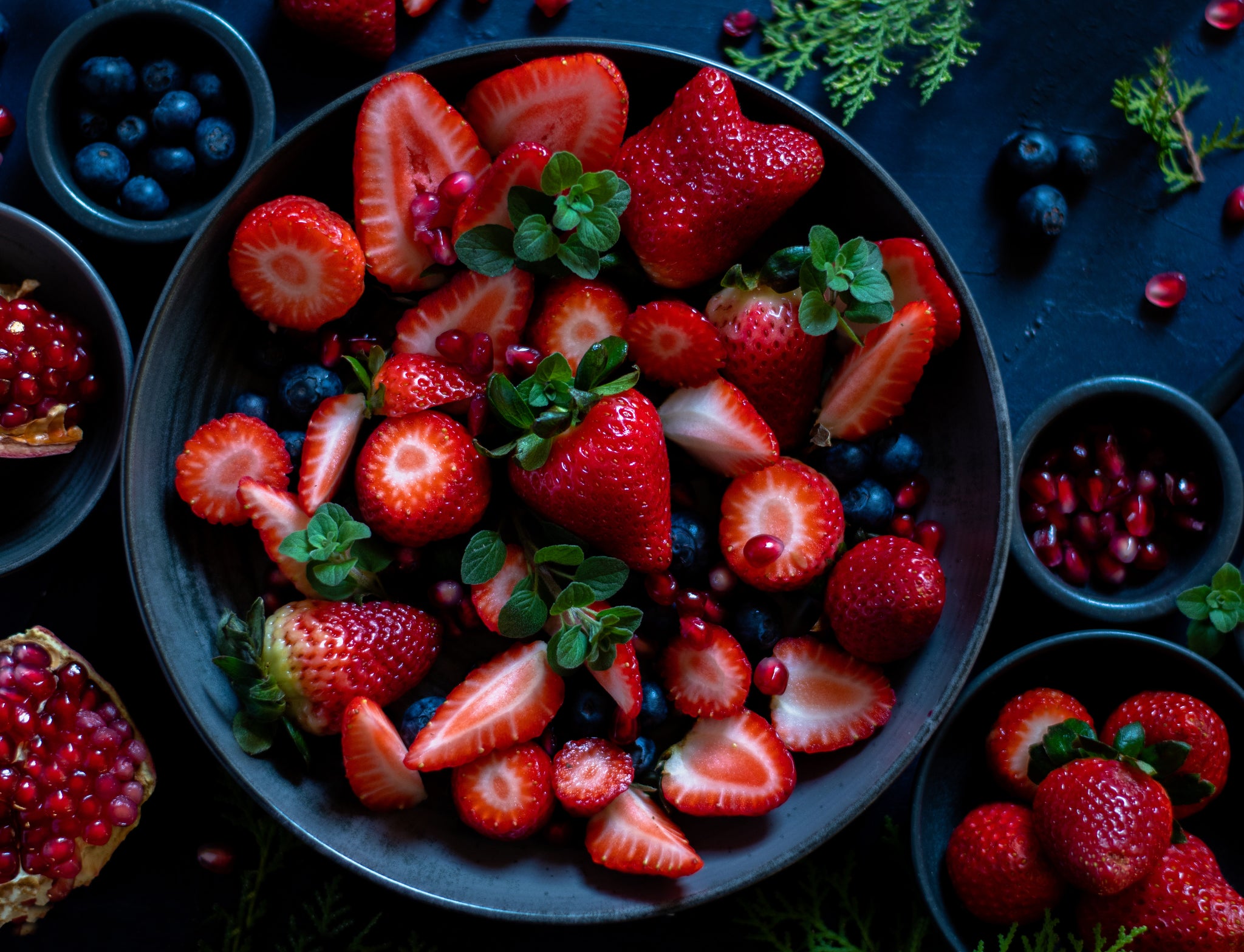 Fresh strawberries and blueberries arranged on a plate against a striking black backdrop.